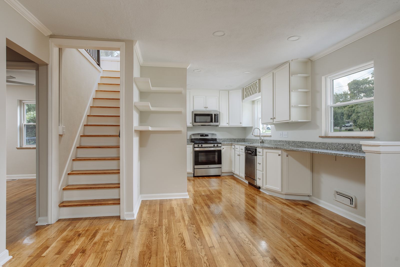Open main level with refinished oak floors, white kitchen cabinetry, and a rebuilt staircase with oak treads