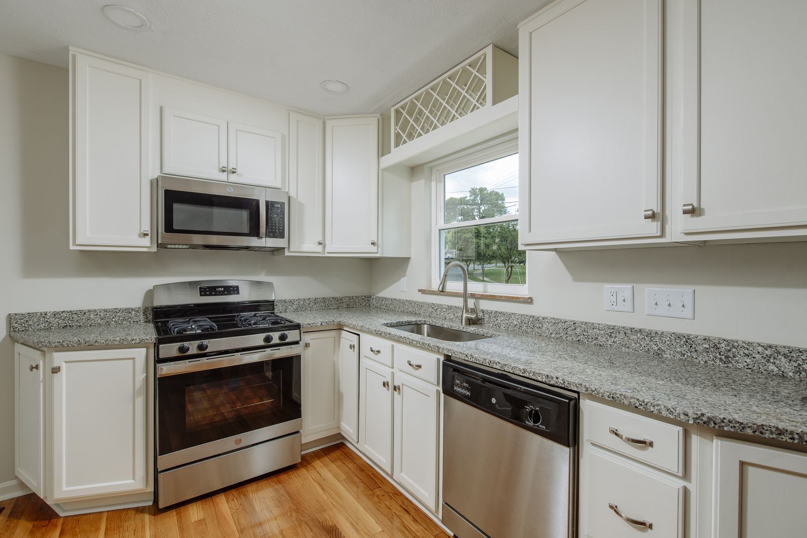 New kitchen with white shaker cabinets, granite countertops, stainless gas range and microwave, and a lattice wine rack over the sink window