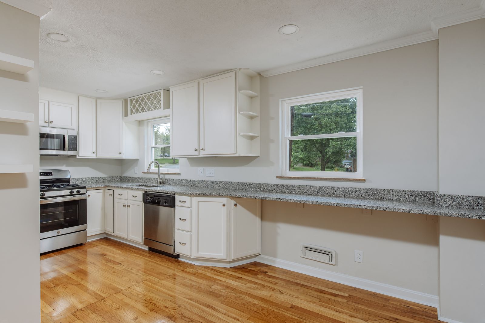 Kitchen with a long granite breakfast bar, white cabinetry, stainless dishwasher, and views to the tree-lined yard