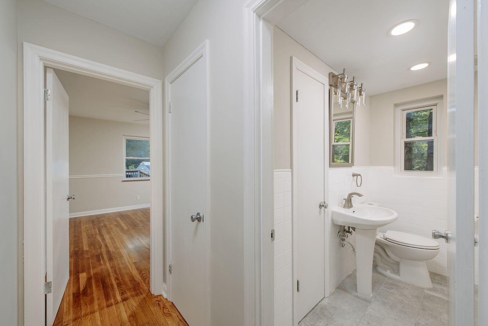 Renovated hall bath with a pedestal sink, white subway tile wainscot, new fixtures, and a view into the adjacent bedroom