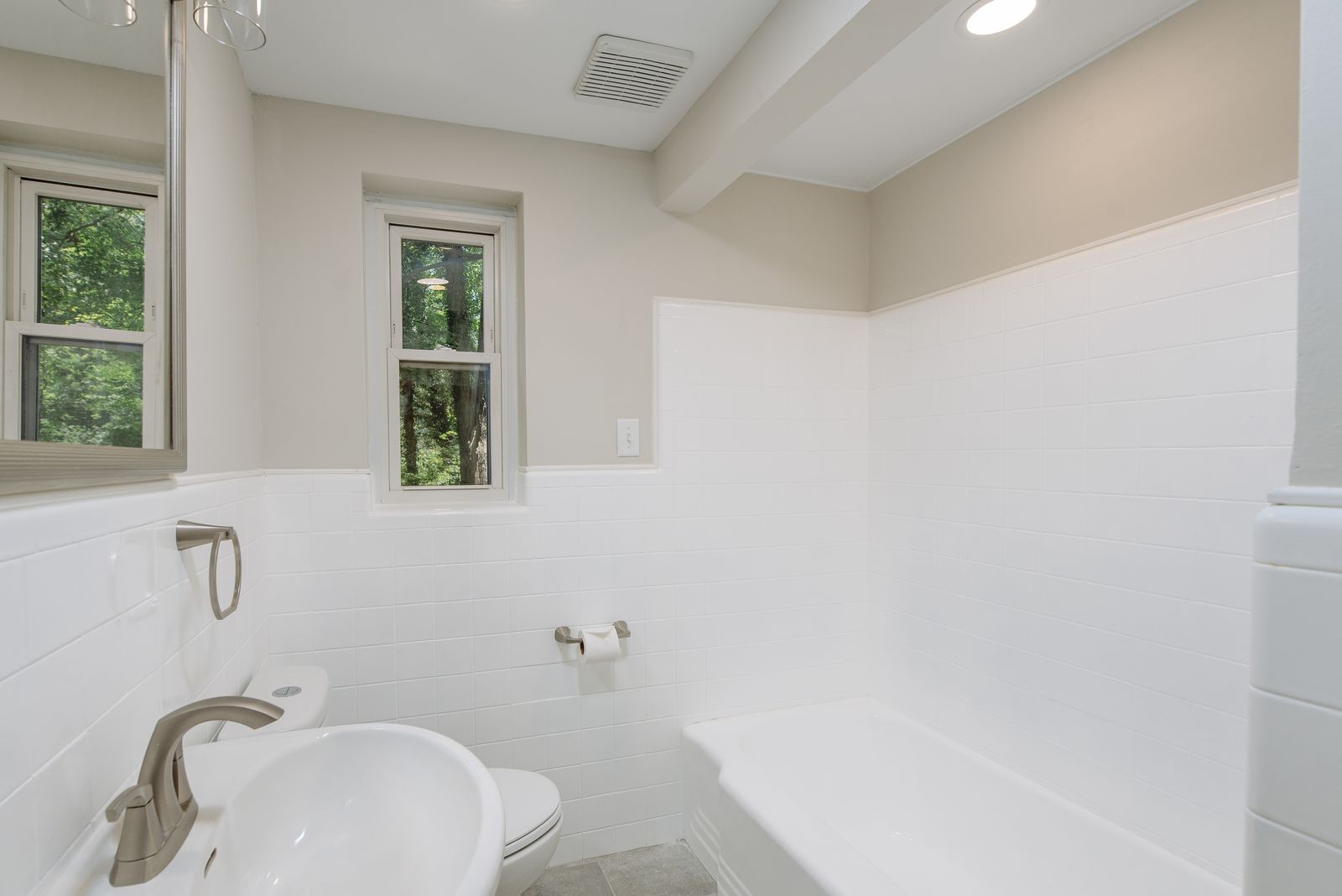 Hall bath tub and shower surrounded in new white subway tile with a window and brushed nickel fixtures