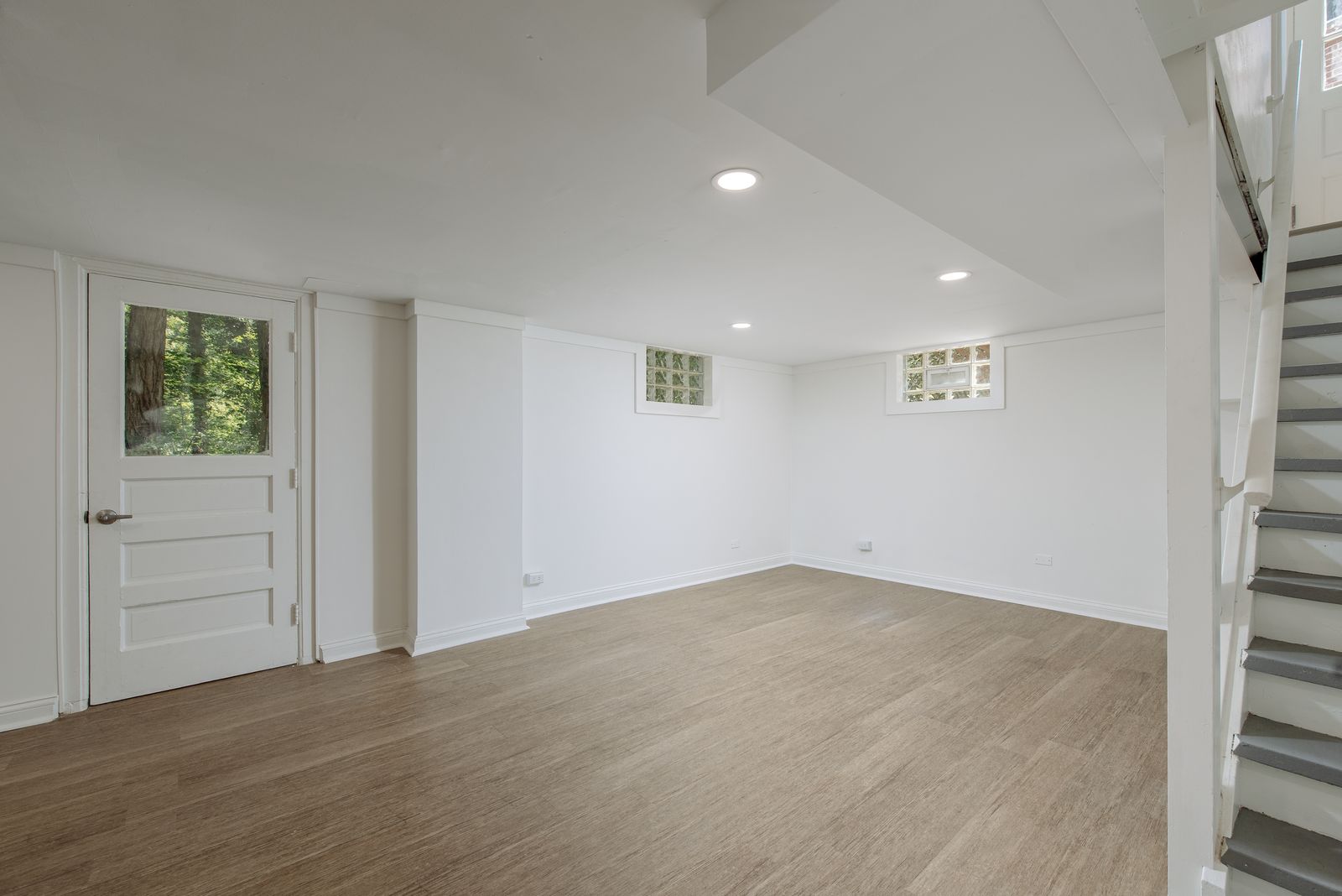 Finished walk-out basement rec room with white paneled walls, recessed lighting, new plank flooring, and an exterior door