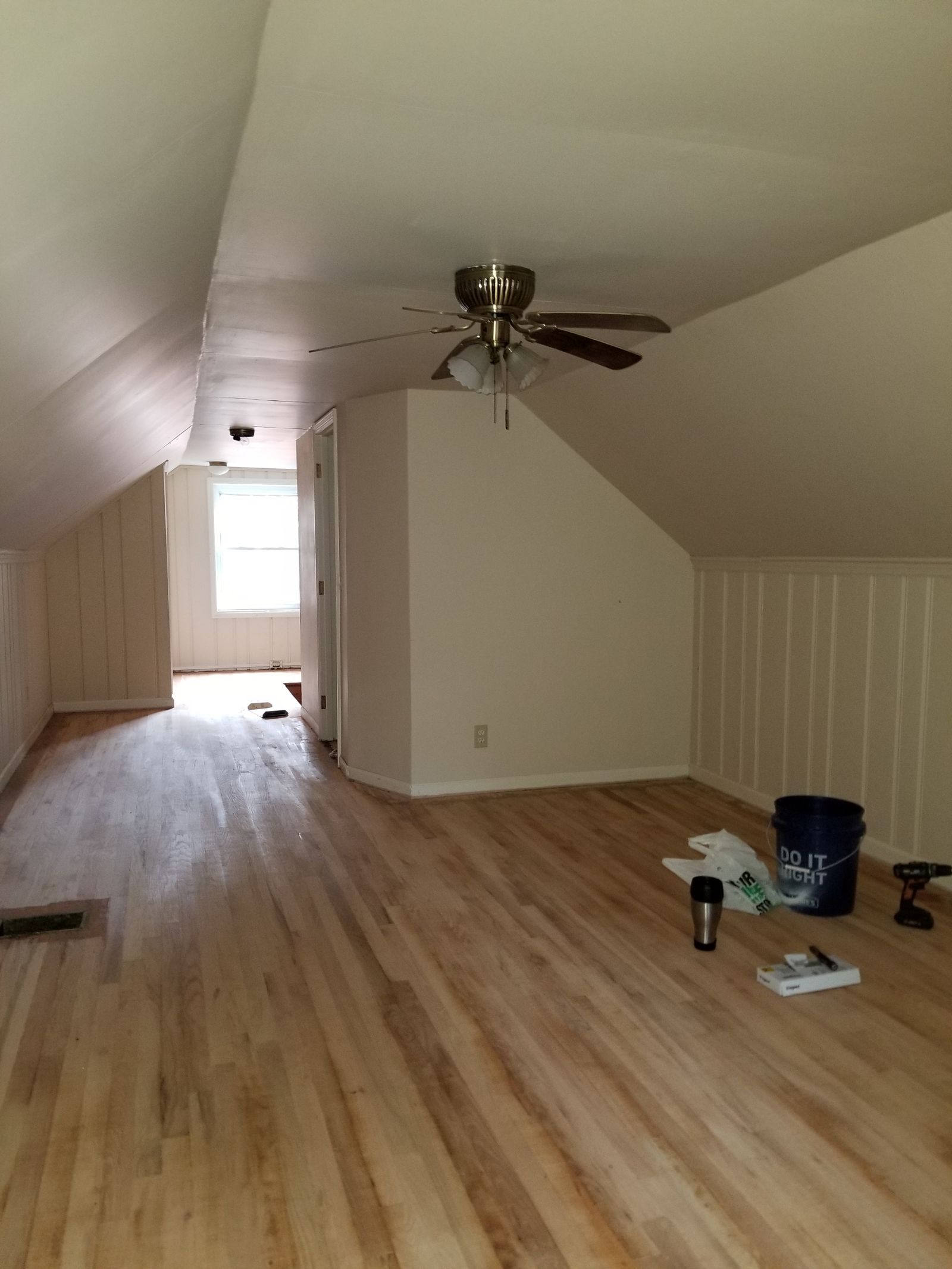 Worn upstairs bedroom with sloped ceilings, scuffed and unfinished oak floors, and a dated brass ceiling fan