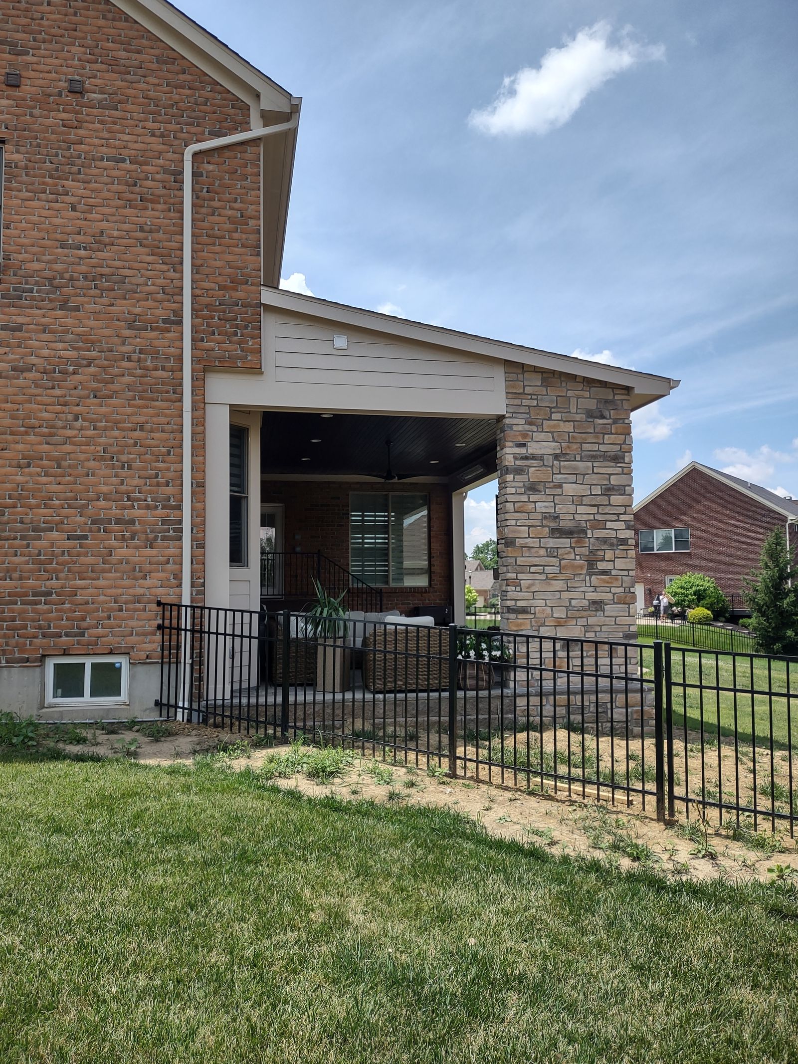 Covered porch addition with stone veneer columns and black aluminum railing viewed from the backyard