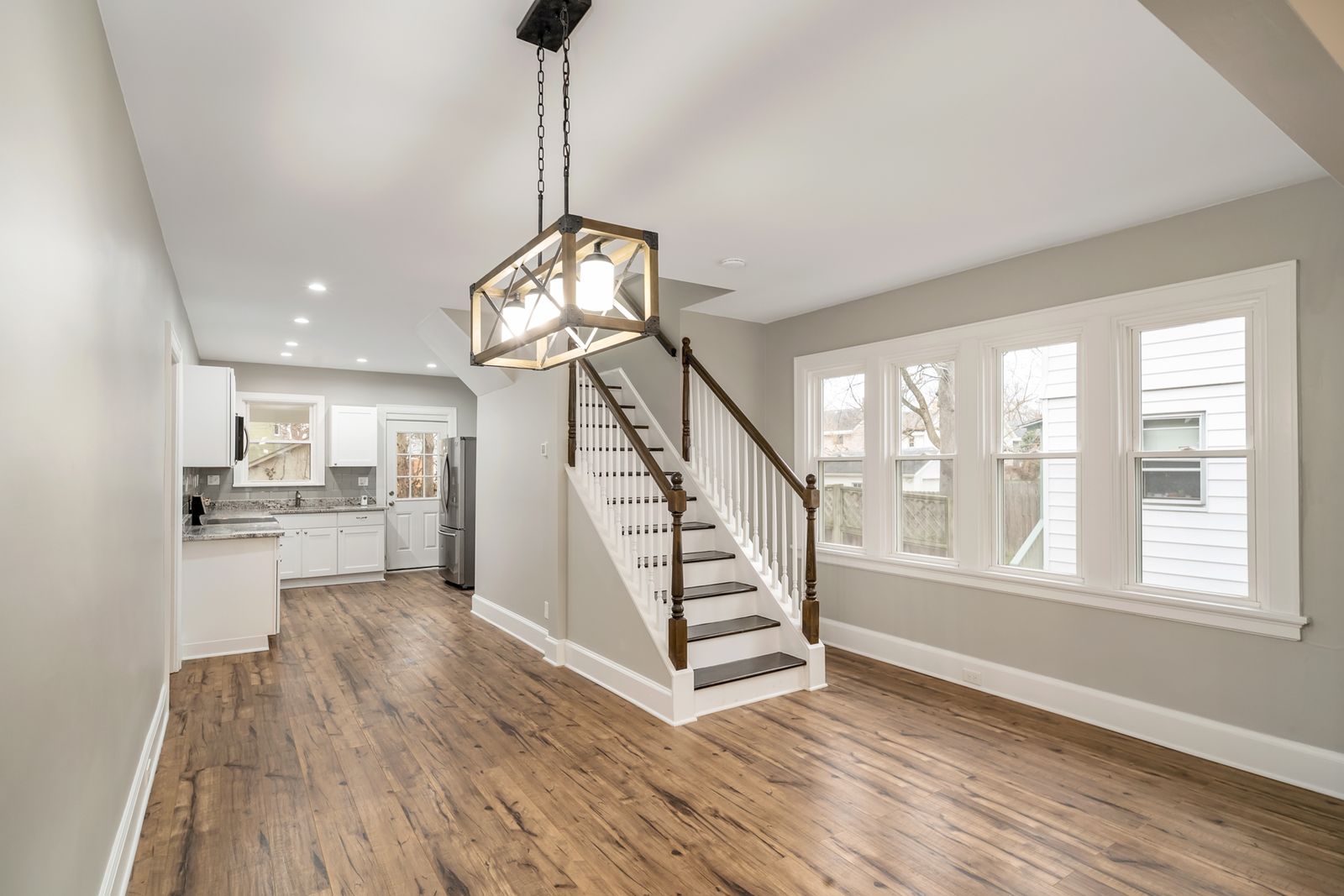 Dining area with a lantern-style pendant light, a refinished wood staircase with white balusters, and the new kitchen beyond