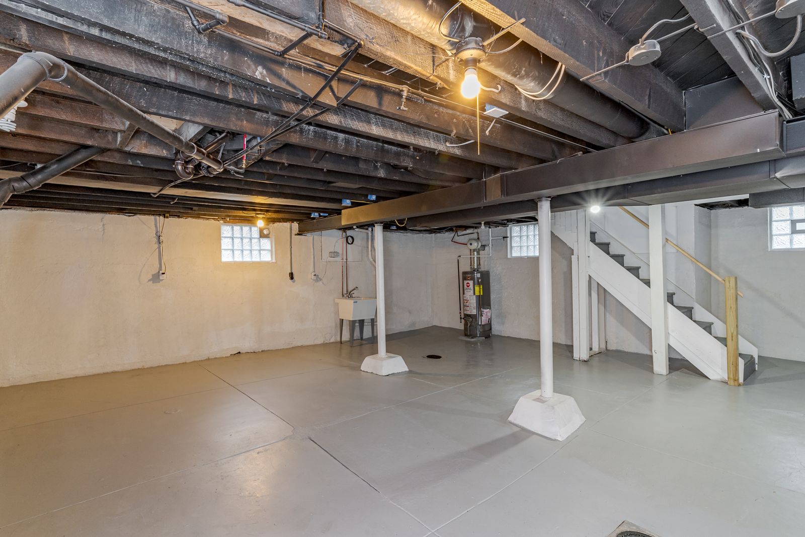 Cleaned-up basement with freshly painted walls and floor, painted ceiling joists, and new support columns