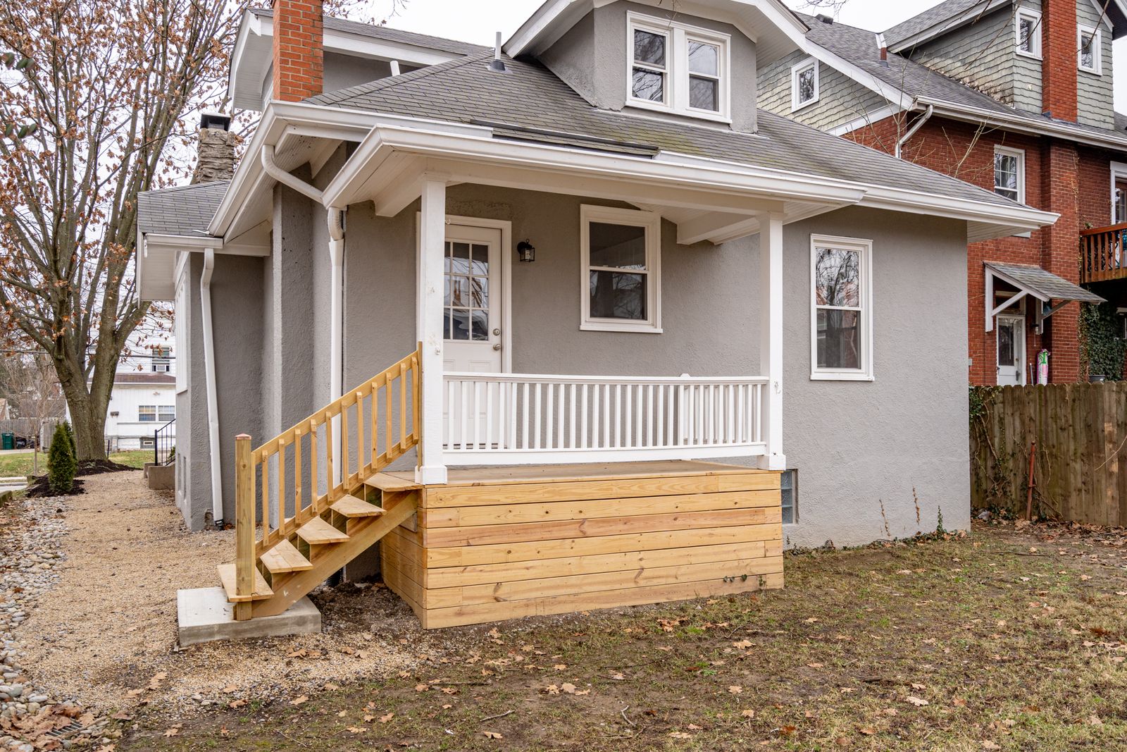Rear of the renovated bungalow showing the new covered back porch with wood skirting, steps, and white railings