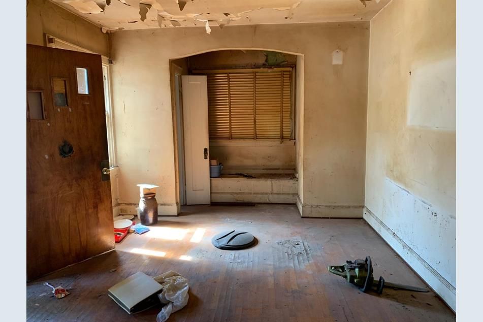Entry area before renovation, with a worn wood front door, peeling ceiling plaster, and tired walls