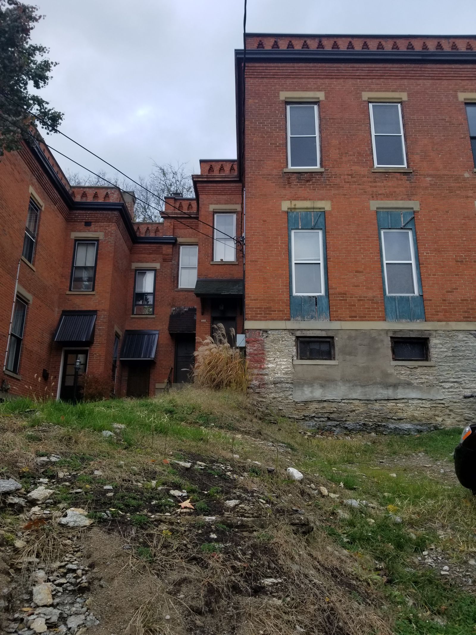 Rear of brick Italianate home before renovation with overgrown yard and boarded windows