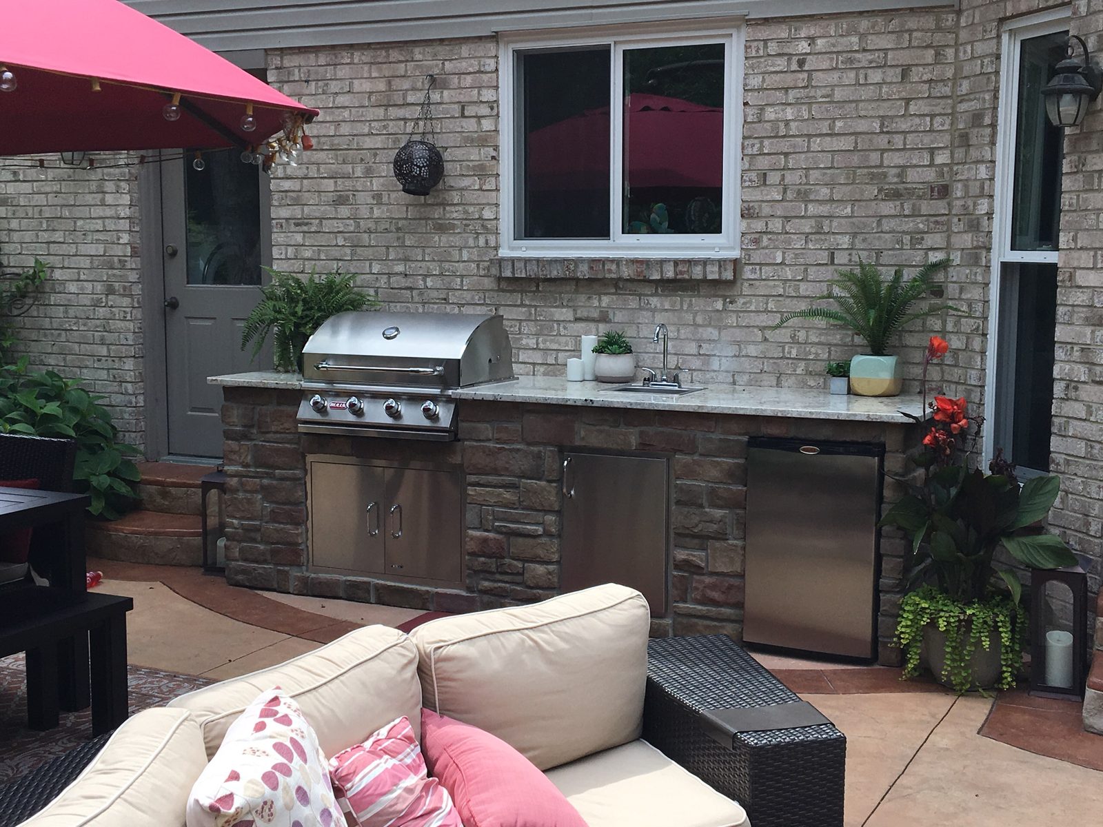 Outdoor kitchen with built-in grill, stone veneer base, and lounge seating on a patio