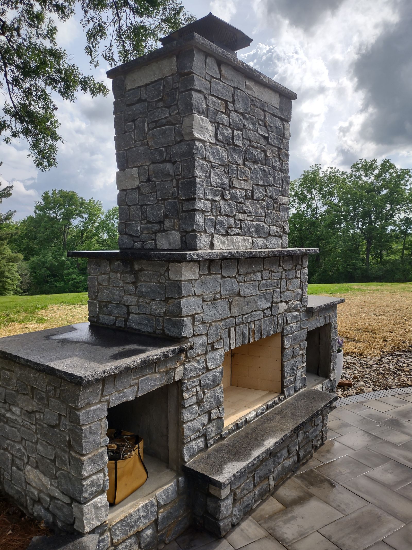 Outdoor stone fireplace with raised hearth and built-in wood storage