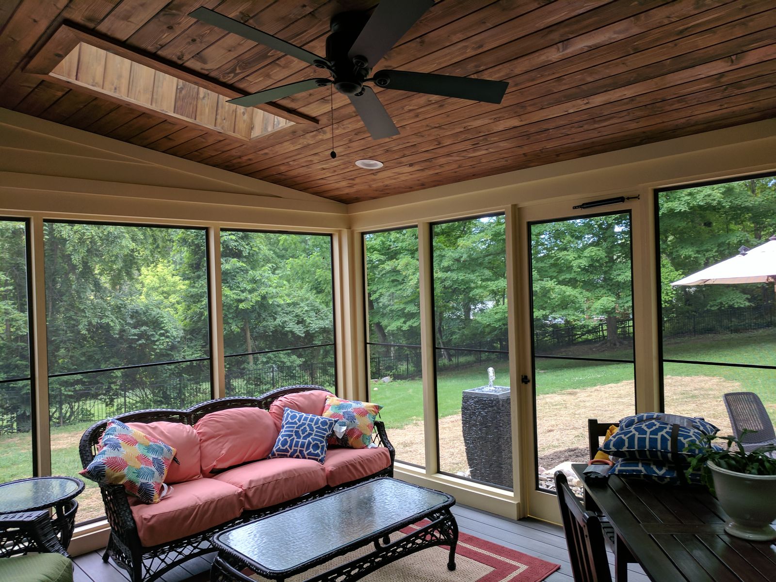Screened porch interior with a wood ceiling, fan, and garden views