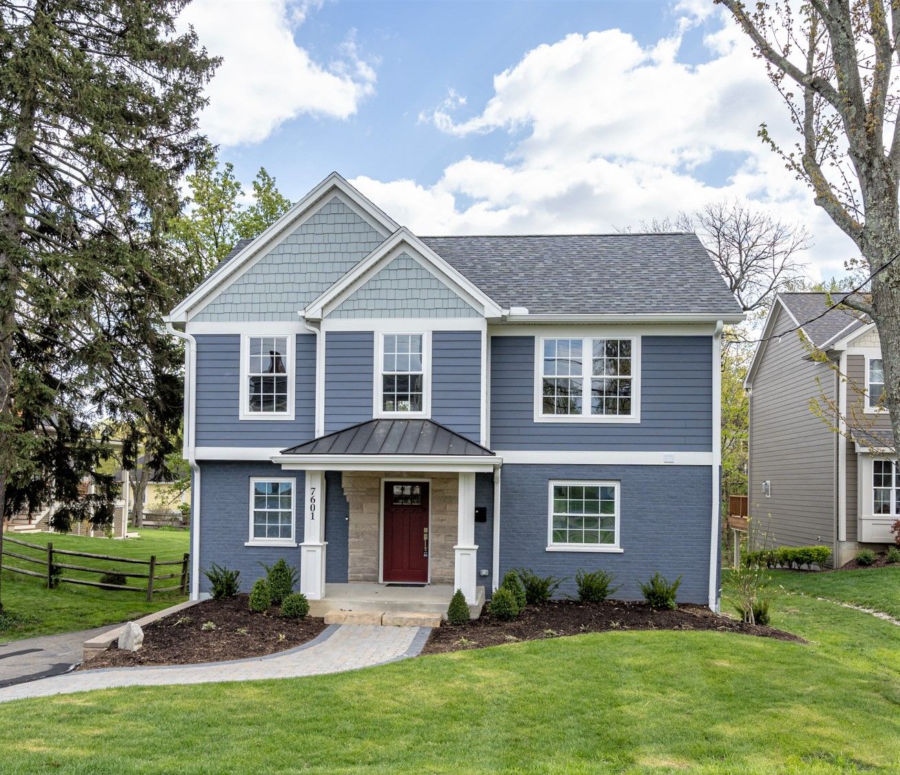 Renovated blue two-story home with white trim, red front door, entry portico, and fresh landscaping