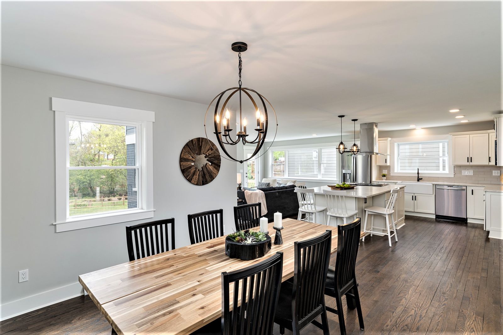 Dining area with farmhouse table, black chairs, and orb chandelier open to the kitchen