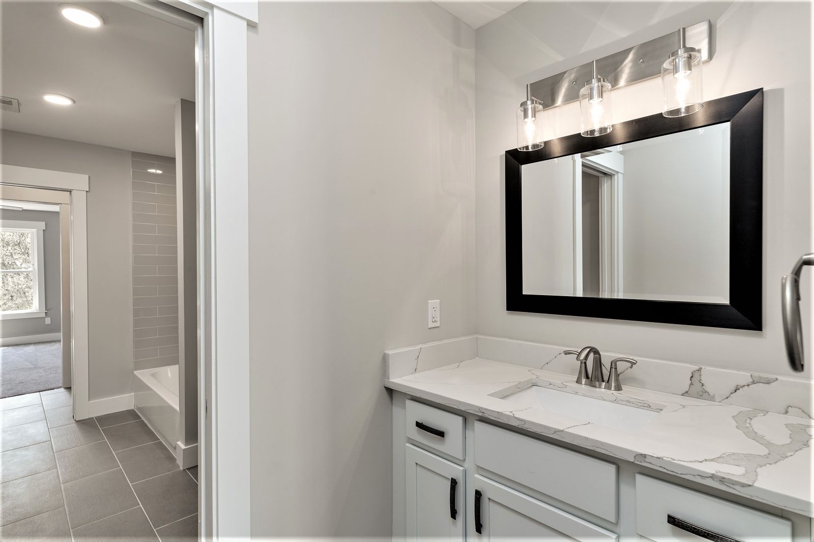 Bathroom vanity with white countertop, dark cabinet, and black-framed mirror