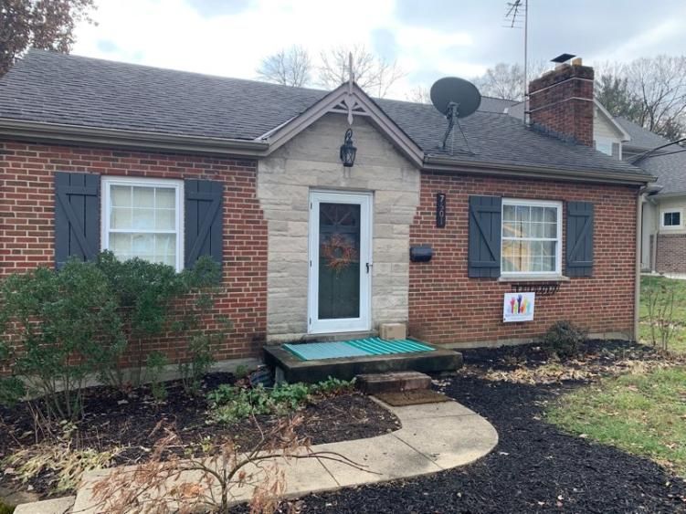 Original single-level brick home with shutters, stone entry surround, and curved front walk