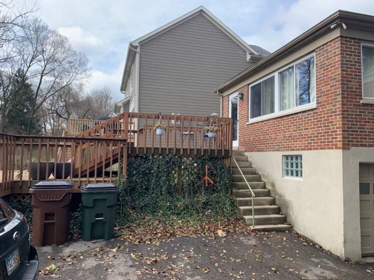 Original rear of the brick home with a weathered wood deck, exterior stairs, and overgrown ivy