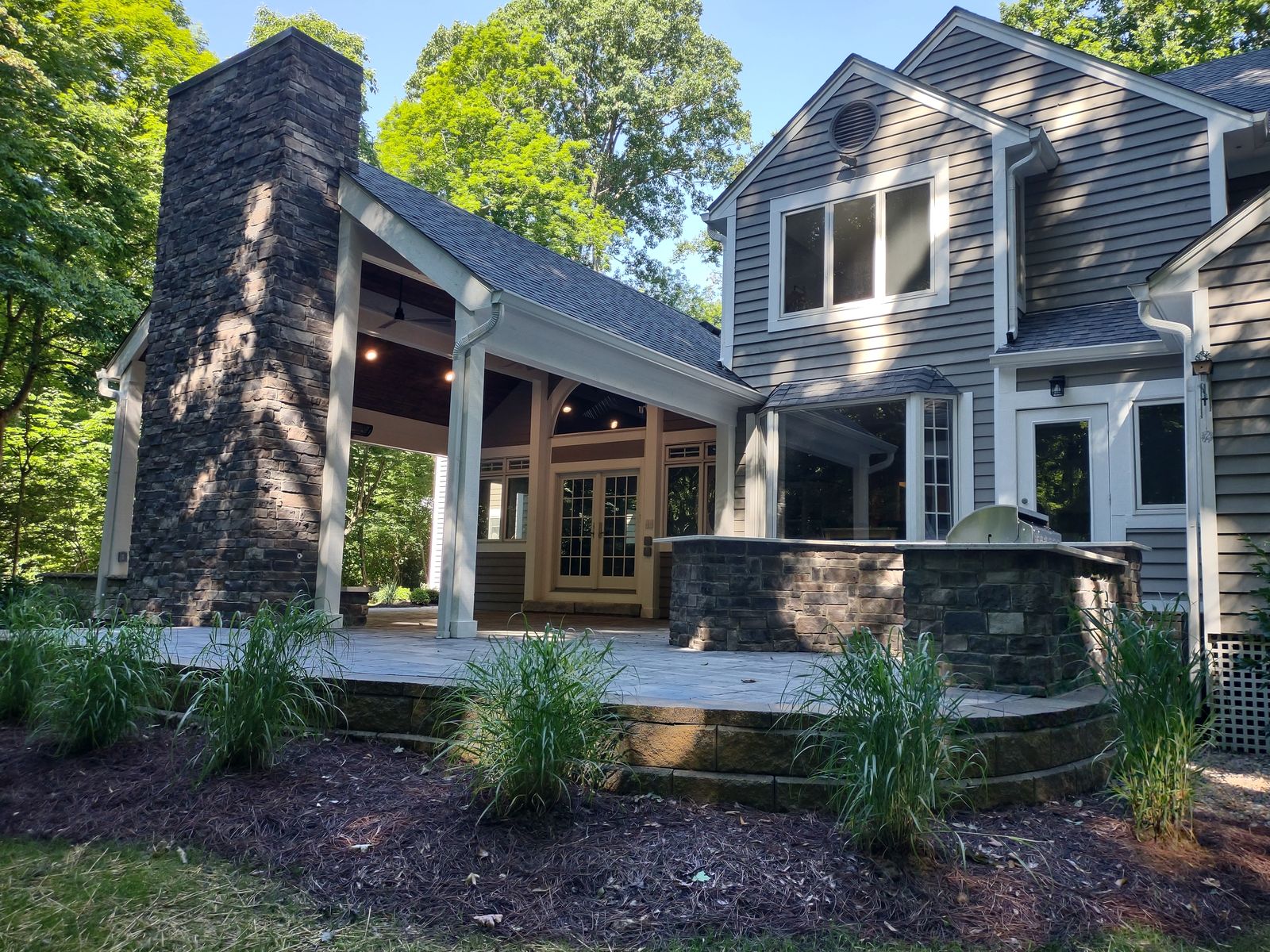 Stone chimney covered porch with grill island and fresh landscaping