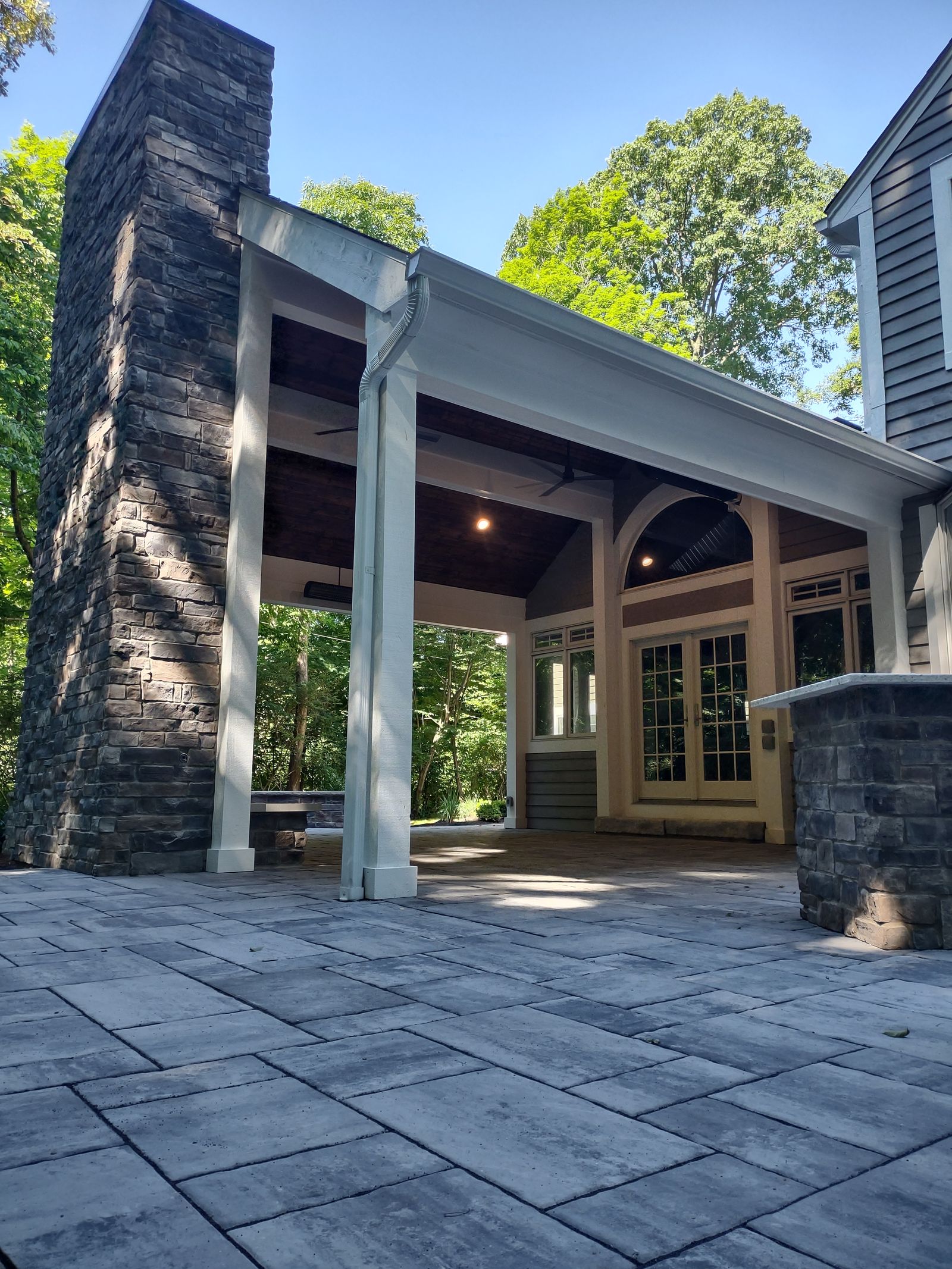 Low angle view of stone chimney and covered porch from paver patio