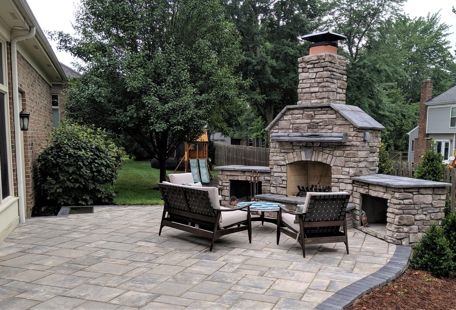 Stone outdoor fireplace with tall chimney and a seating area on a paver patio