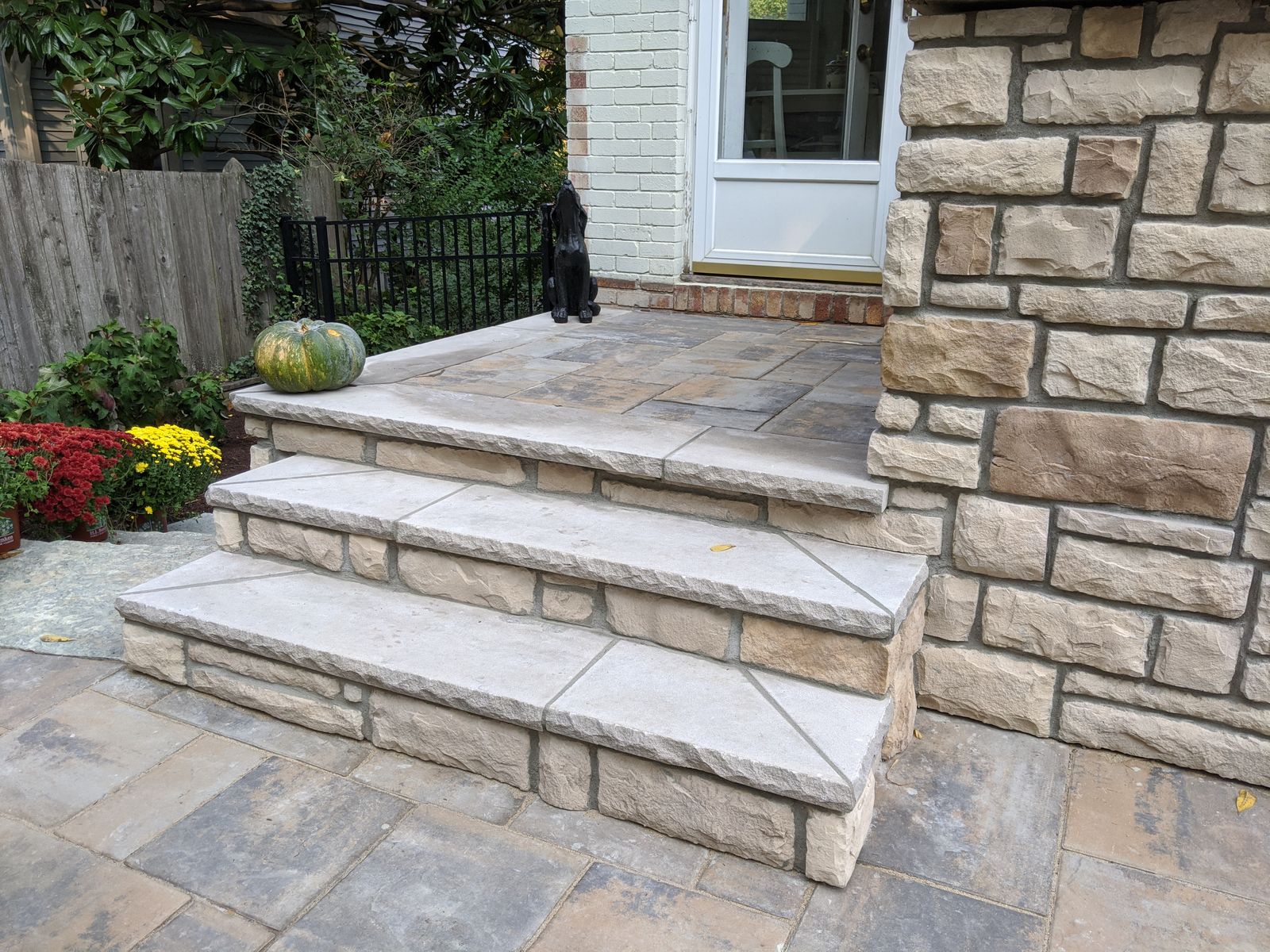 Wide cut-stone steps between a stone wall and a paver patio
