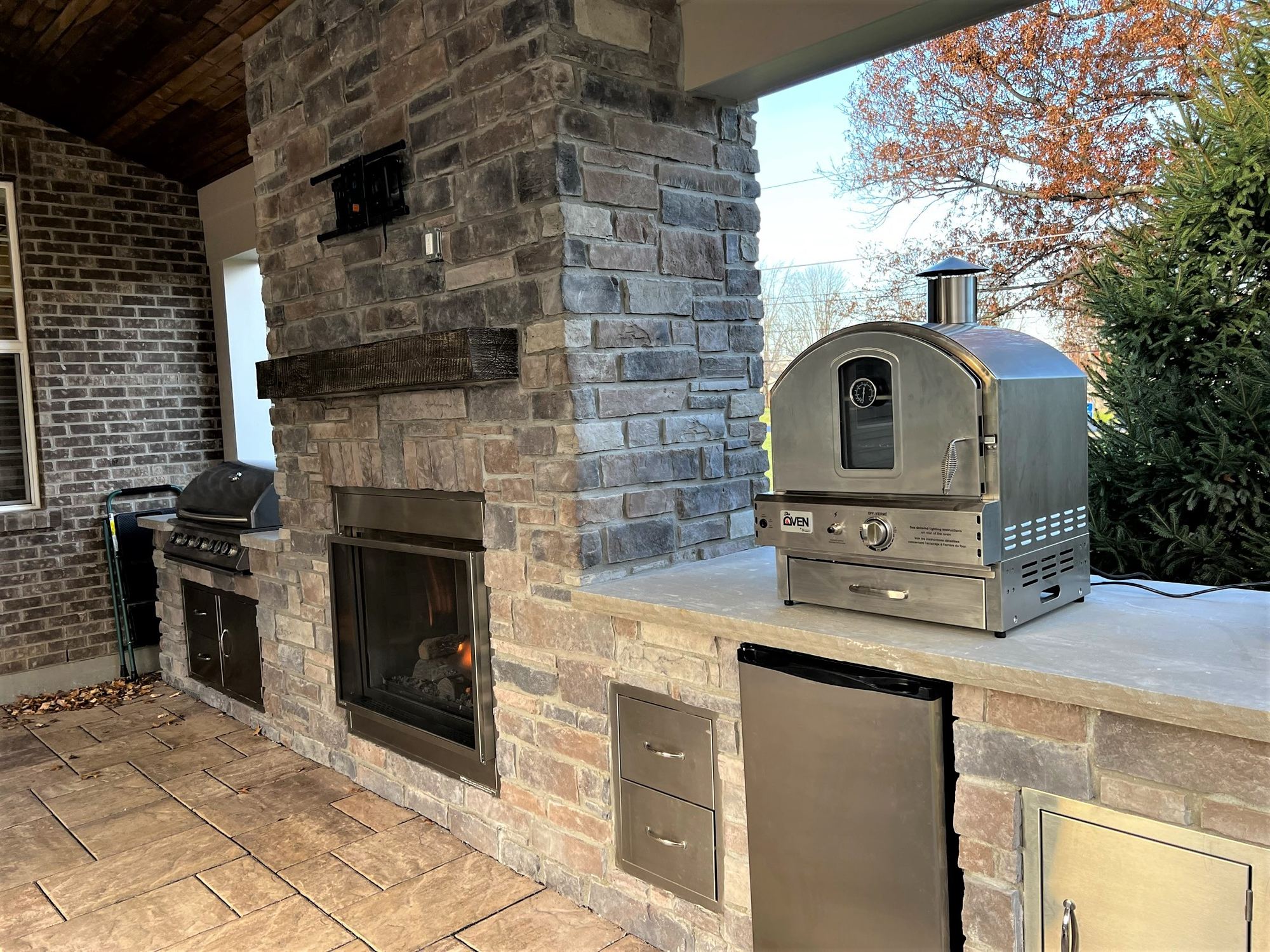 Outdoor kitchen with built-in grill, pizza oven, and stone fireplace under a covered porch