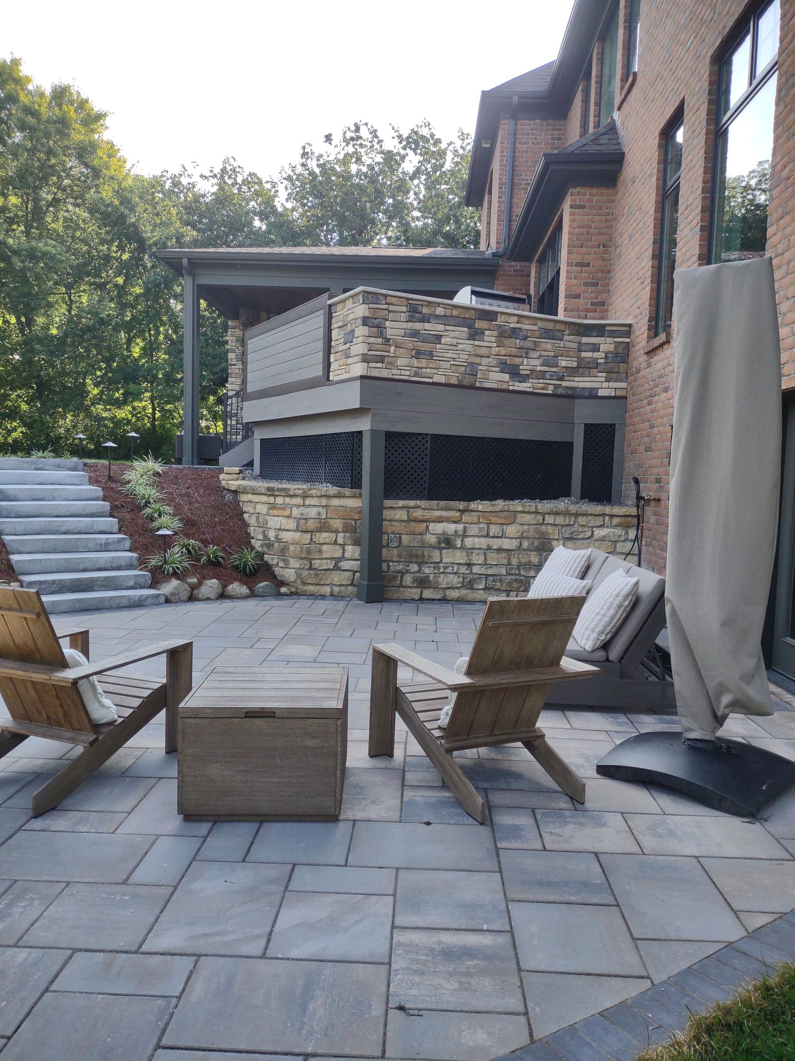 Paver patio lounge facing two-story deck with stone retaining wall