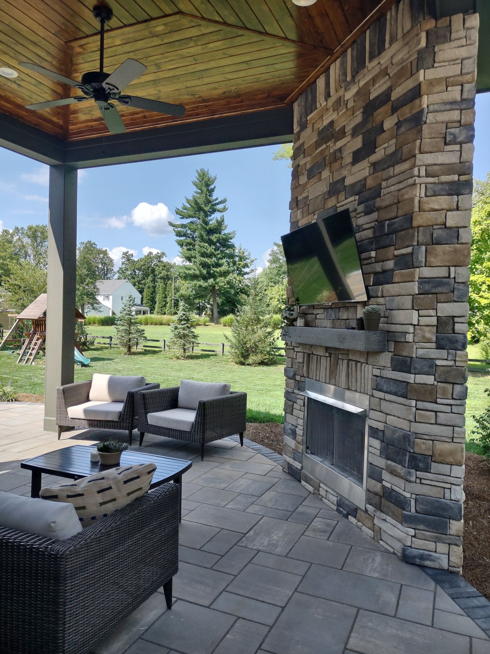 Covered pavilion with stone fireplace, mounted TV, and backyard view