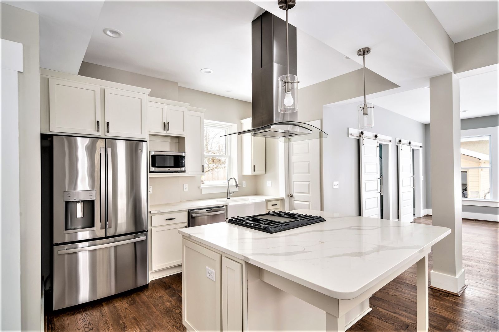 Renovated kitchen with white cabinetry, island cooktop, and stainless appliances